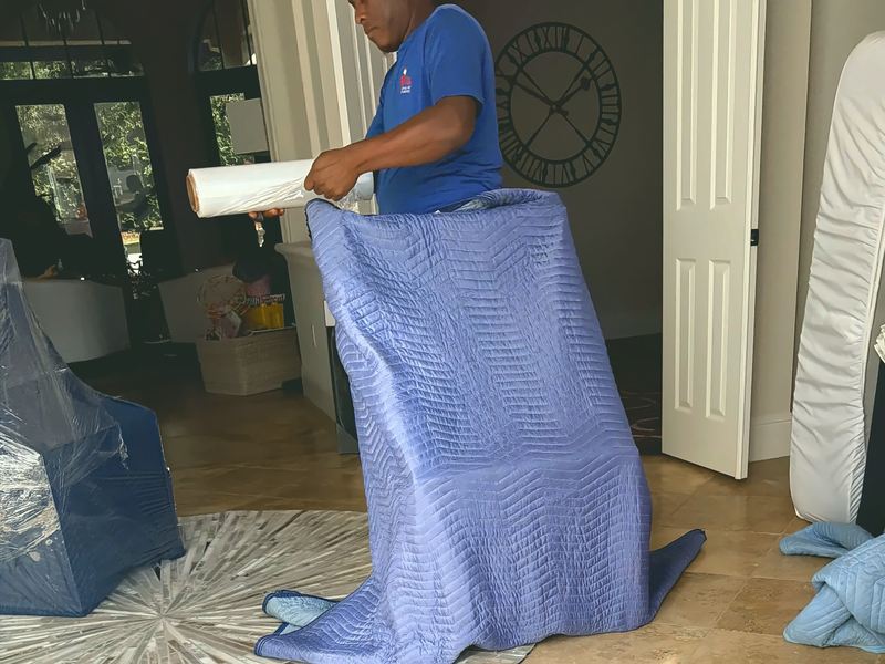 Mover shrink-wrapping a blanket-covered piece of furniture