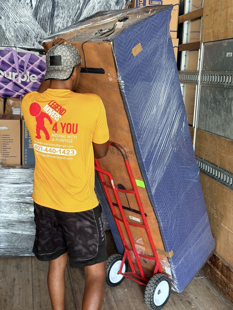 Mover moving a tall padded item on a red hand truck