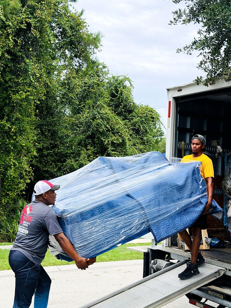 Movers carrying a padded, wrapped sofa up the truck ramp