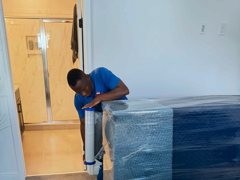 Legend Movers 4 You mover stretch-wrapping a large padded item in a hallway before the move