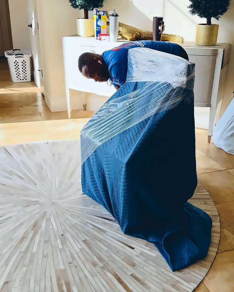 Legend Movers 4 You mover securing a blue moving blanket around furniture with shrink wrap