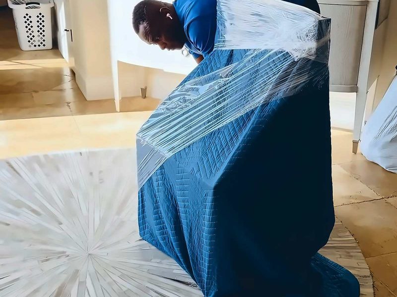 Legend Movers 4 You mover securing a blue moving blanket around furniture with shrink wrap