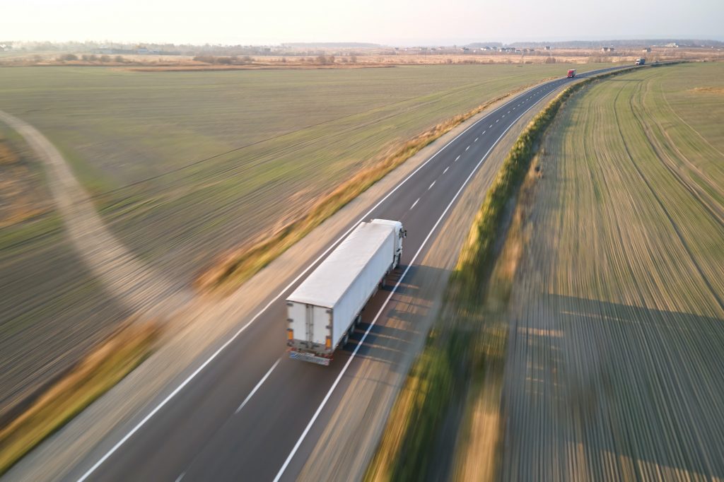 Aerial view of blurred fast moving semi-truck with cargo trailer driving on highway hauling goods in