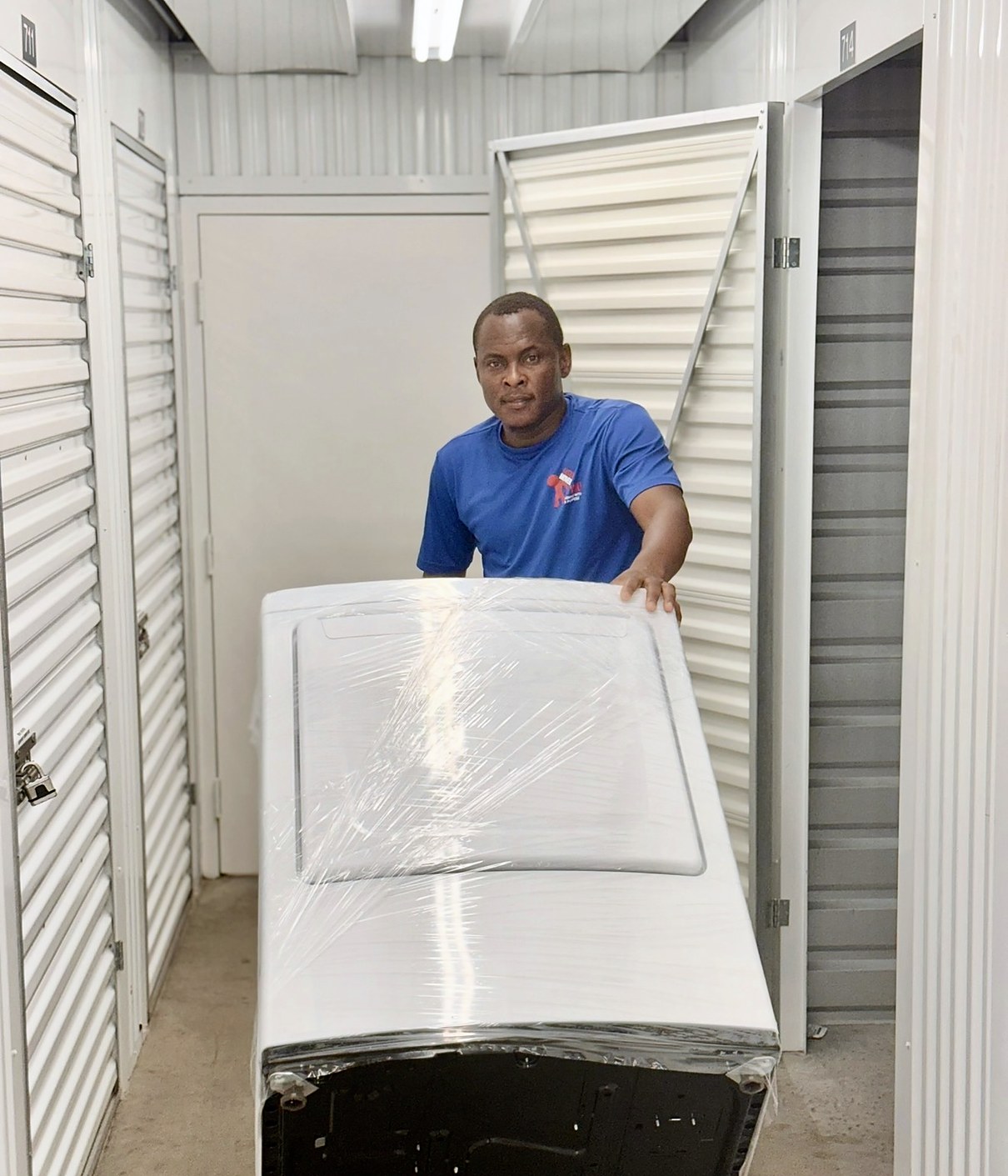 Legend Movers 4 You mover in a blue uniform shirt with a stretch-wrapped washer in a storage facility hallway